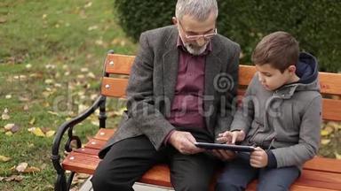 爷爷和孙子一起在公园里度过时光.. 他们坐在长凳上用平板电脑